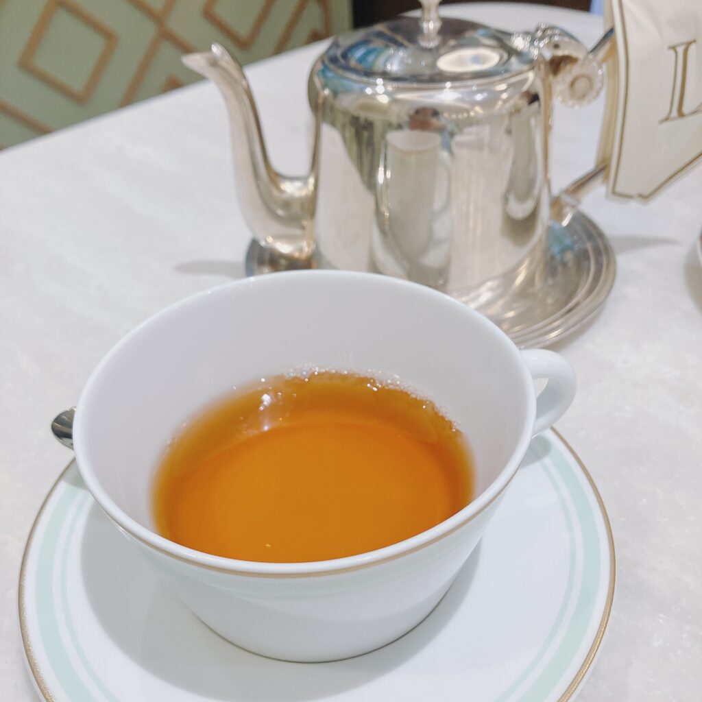ラデュレのティーセット。銀色のティーポットが奥にあり、手前には白いカップ＆ソーサーに透明感のあるオレンジ色の紅茶が注がれている。カップとソーサーの縁にはミントグリーンとゴールドのラインが入っている。