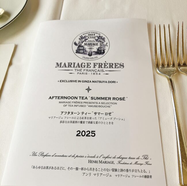 マリアージュフレール銀座松屋通り店のアフタヌーンティーメニュー。中央に「MARIAGE FRERES」のロゴ、その下に「AFTERNOON TEA "SUMMER ROSÉ"」と英語で表記され、さらに日本語で「アフタヌーンティー "サマー ロゼ"」と続く。一番下には「2025」と大きく年号が記載されている。上部には「EXCLUSIVE IN GINZA MATSUYA DORI」と書かれており、銀座松屋通り店限定のメニューであることがわかる。右隣には金色のフォークが2本並べられている。