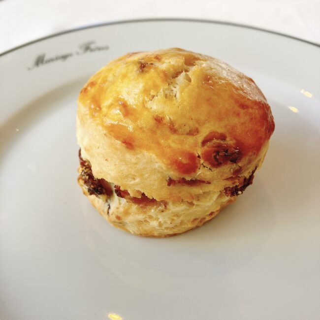 焼き色が美しい丸いレーズンスコーンが白い皿に置かれている。表面は照りがあり、レーズンが散見される。皿の縁には筆記体でマリアージュフレールと書かれており、黒いラインが入っている。