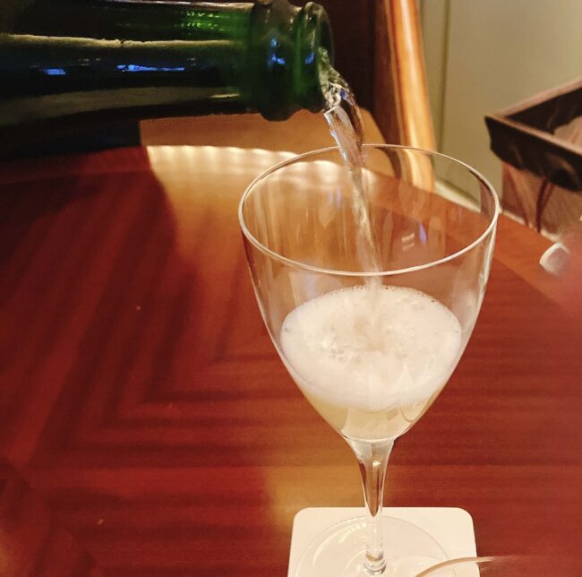 緑色のボトルからワイングラスに注がれる、泡立つ飲み物。ホテルのスタッフが飲み物を注いでいる様子。