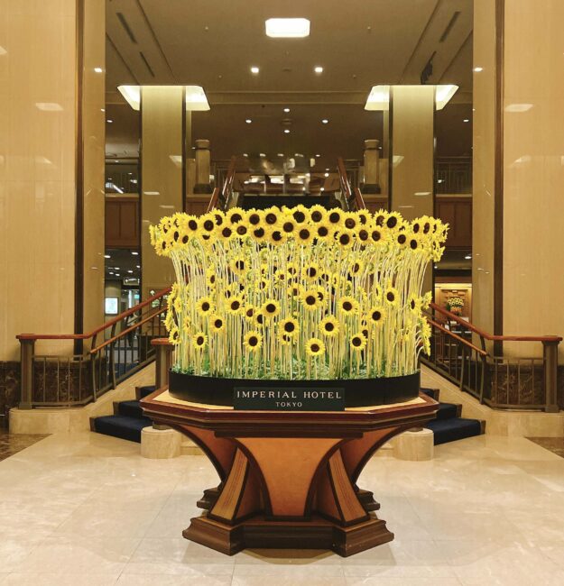 帝国ホテルのロビーにある、円形の大きな装花。無数のひまわりが放射状に並べられ、「IMPERIAL HOTEL TOKYO」と書かれた黒い帯で囲まれている。