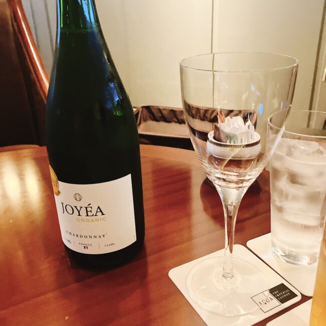 「JOYÉA ORGANIC」の白ワインボトルと、ワイングラス、氷入りグラスがテーブルに置かれている。グラスの下には「IMPERIAL LOUNGE AQUA」のロゴ入りコースターが見える。