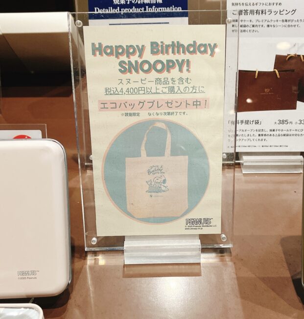 帝国ホテルのホテルショップに掲示された、スヌーピーのキャンペーン告知ポスター。「Happy Birthday SNOOPY!」の文字と、「スヌーピー商品を含む税込4,400円以上購入の方にエコバッグプレゼント中！」の案内が書かれている。