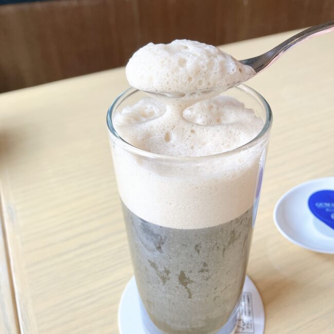 ザ ロイヤルパークホテル アイコニック 東京汐留で提供された、グラスに入ったコーヒークレマ。上にはきめ細かな泡が乗っており、スプーンで泡をすくっている。









