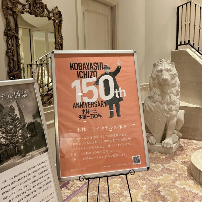 第一ホテル東京のエントランス付近。阪急電鉄創業者である小林一三の生誕150周年を記念した大きなポスターが置かれている。ポスターの横にはライオンの像があり、奥にはホテルの階段が見える。