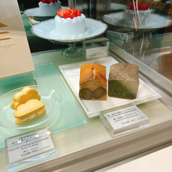 ホテル椿山荘東京のショップ「セレクションズ」にあるショーケースの写真。棚には、栗のパウンドケーキ（抹茶と和栗の2種類）や、バターレーズンサンドクッキー「東京～海と雲～サンド」が並んでいる。奥にはイチゴのデコレーションが施されたホールケーキのサンプルも見え、「ホールケーキは予約制」の注意書きがある。