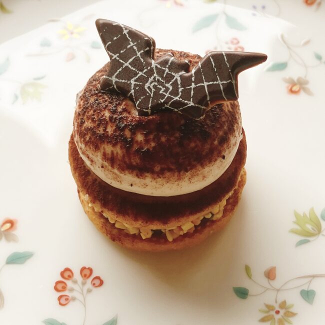 ホテル椿山荘東京のハロウィンアフタヌーンティーのスイーツ。「コウモリの栗サブレ」。コウモリ型のチョコレートが乗ったマカロン型の栗サブレで、マロンガナッシュが挟まれている。