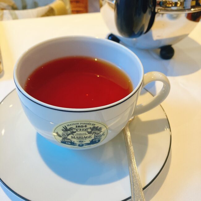 マリアージュフレールのティーカップに入った、赤褐色の紅茶「ミッドナイトマジック」。黒茶ベースにサフラワー(紅花)の花びらが散りばめられ、フルーティーで甘いキャンディのような香りがする。