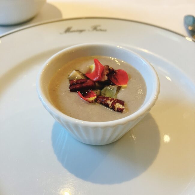 マリアージュフレールのアフタヌーンティー「フルムーンパーティー」のセイボリー、「ノクターン オリエンタル香るキノコのヴルーテ」。白いカップに入ったキノコ風味のヴルーテの上には、赤いバラの花びらとナッツが飾られている。