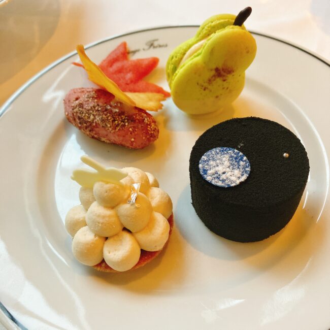 マリアージュフレール「フルムーンパーティー」のスイーツプレート。黒い円形のムースは満月、白いタルトはお月見うさぎ、洋梨型マカロン、赤い木の葉形チップが飾られた焼き芋、の四種類が美しく盛り付けられている。