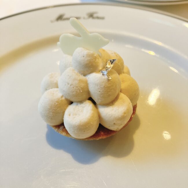 マリアージュフレール「フルムーンパーティー」のスイーツ、「緑茶フルムーンパーティーのタルト 観月の宴」。白いクリームのドーム状タルトのてっぺんにお月見うさぎを模した白いチョコレートが飾られ、銀箔が添えられている。
【観月の宴】緑茶フルムーンパーティーのタルト
満月をイメージした愛らしい見た目のタルトです。てっぺんには、お月見のテーマに合わせた「お月見うさぎ」がちょこんと乗っています。