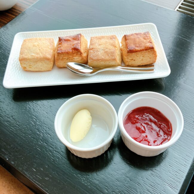 コンラッド東京のアフタヌーンティーで提供されるスコーン。四角いプレーンスコーンが4つ白い長方形の皿に並べられ、手前にはバターとイチゴジャムと思われる赤いジャムが白い小皿に盛られている。