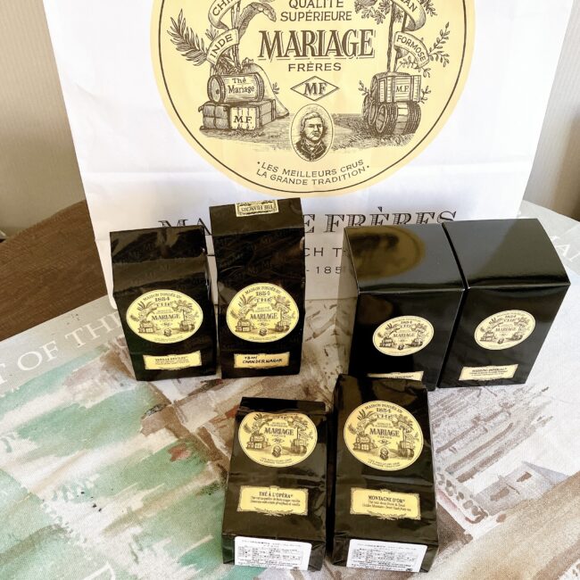 マリアージュフレール(マリフレ)の6銘柄福袋の中身の写真。黒いパッケージの紅茶が6箱と、大きなマリフレの紙袋が写っている。様々な種類の紅茶を試したい人向けの福袋。