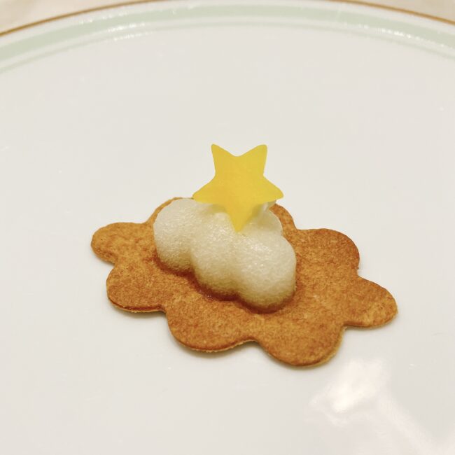 ラデュレ日比谷の『星の王子さま』コラボアフタヌーンティーのセイボリー「夜の砂漠」。雲の形をしたクッキーの上に白いクリームと黄色い星型の飾りが乗っている。濃厚なチキンストックと黄色人参を使用している。