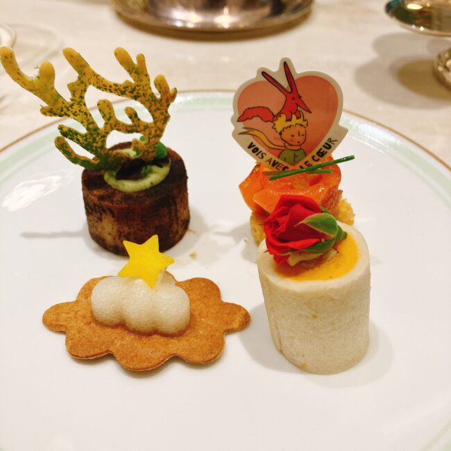 ラデュレ日比谷の『星の王子さま』コラボアフタヌーンティーのセイボリー4種。別皿に盛り付けられたメニューは、バオバブの木を模したじゃがいもとセップ茸のタルト、バラの飾りが乗ったチキンとバターナッツのロールサンド、星の王子さまのイラスト入りプレートが添えられたスモークサーモンのブリオッシュ、雲のクッキーなど。