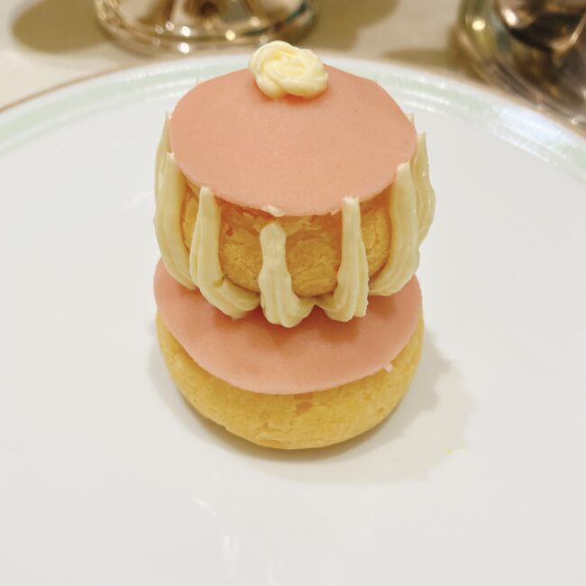 ラデュレ日比谷『星の王子さま』コラボアフタヌーンティーのミニパティスリー「ルリジューズ・ローズ・フランボワーズ」。ピンク色の丸いシュー生地が2段重ねになっており、間にはクリームが絞られている。フランスの伝統菓子ルリジューズをローズとフランボワーズで華やかに表現している。