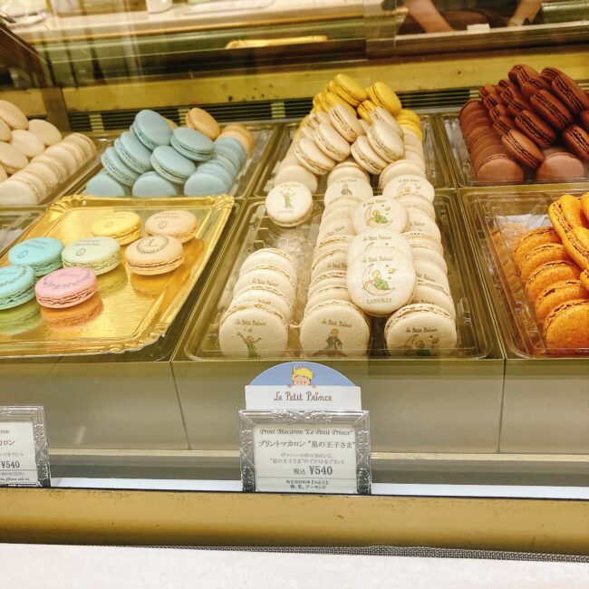 ラデュレ日比谷店の店頭にあるマカロンのショーケース。ケースの中央には「Le Petit Prince」と書かれたPOPがあり、星の王子さまがプリントされたクリーム色のプリントマカロンが並んでいる。その他に、パステルブルーやピンク、ブラウンなど数種類のマカロンが見える。