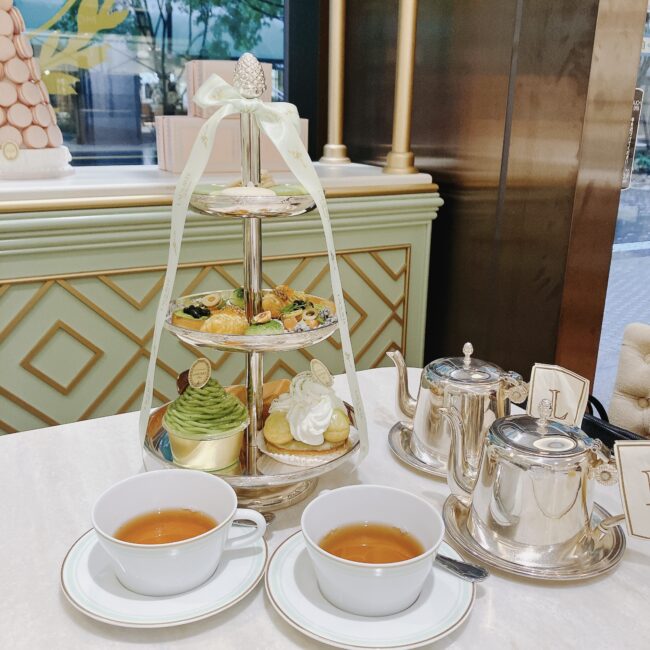 ラデュレ日比谷店のアフタヌーンティー。白とミントグリーンを基調とした店内で、シルバーのティースタンドにはマカロン、モンブラン、エクレアなどのスイーツが並ぶ。手前には紅茶の入った白いティーカップと銀のティーポット。