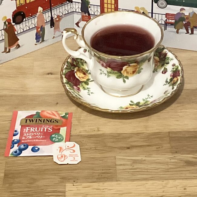 トワイニング アドヴェントカレンダー2025、5日目の「ストロベリー＆フルーツ」。紅茶が注がれた花柄の英国風ティーカップと、ロンドンの街並みの背景。酸味のある赤い水色のフルーツティー。