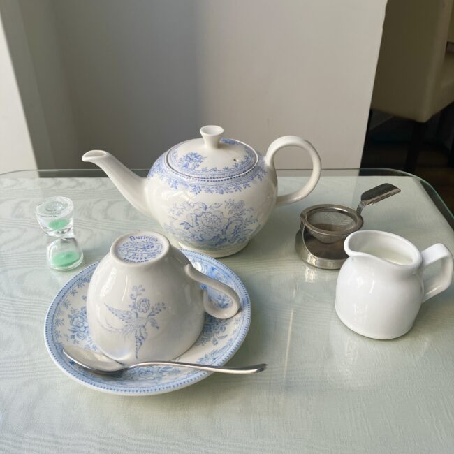 ジュリスティールームの英国式ティーセット全景。白いポット、逆さまに置かれたブルー&ホワイトのカップ、ミルクジャグ、砂時計、ティーストレーナーが並んでいる。