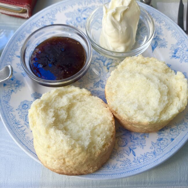 ジュリスティールームのカントリースコーンを縦に割った写真。スコーンの内側のふかふかした生地が見える。クロテッドクリームとジャムが添えられている。