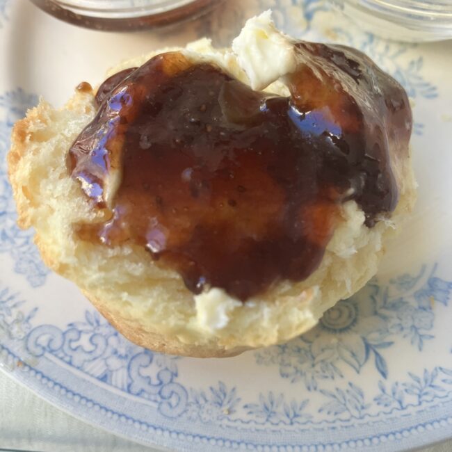 ジュリスティールームのカントリースコーンに、デヴォン式でクロテッドクリームとジャムを乗せた写真。スコーンは半分に割られており、たっぷりのジャムがクリームの上に載っている。