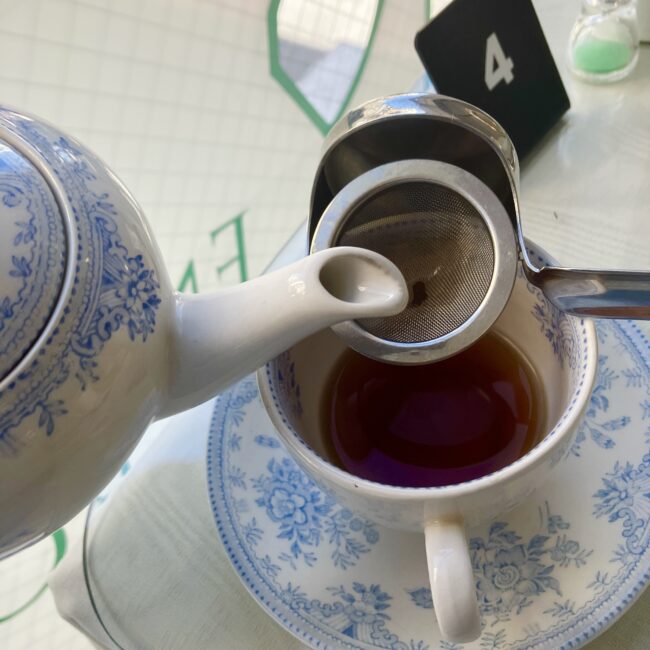 ティーポットからカップへティーストレーナー を通して紅茶を注いでいるところ。英国の伝統的な作法 を示す写真。