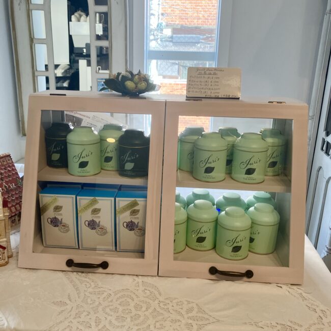 ジュリスティールームのオリジナル紅茶商品の陳列棚。ミントグリーンの缶 や箱入りの紅茶が並べられている。