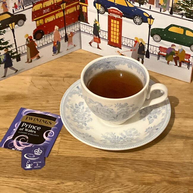 トワイニング アドヴェントカレンダー2025、６日目の「プリンスオブウェールズ」。紅茶が注がれた花柄の英国風ティーカップと、ロンドンの街並みの背景。酸味のある赤い水色のフルーツティー。