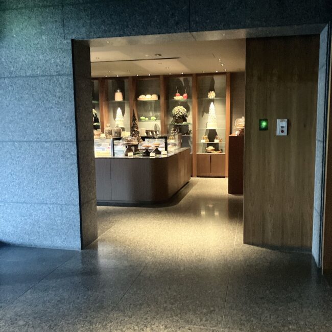 パークハイアット東京2階、ペイストリーブティックの入り口。重厚な石壁の開口部から、温かい照明に照らされた洗練された店内が見える。ショーケースには色鮮やかなケーキや焼き菓子が並んでいる。