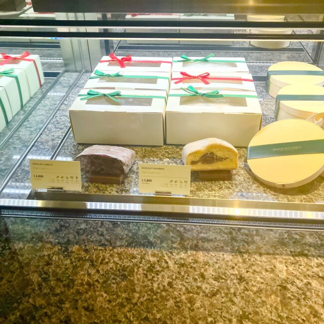 ギフトボックス入りのシュトレン(チョコ、マロン)。クリスマスらしいリボンがかかった箱と、断面が見えるように展示された商品見本。