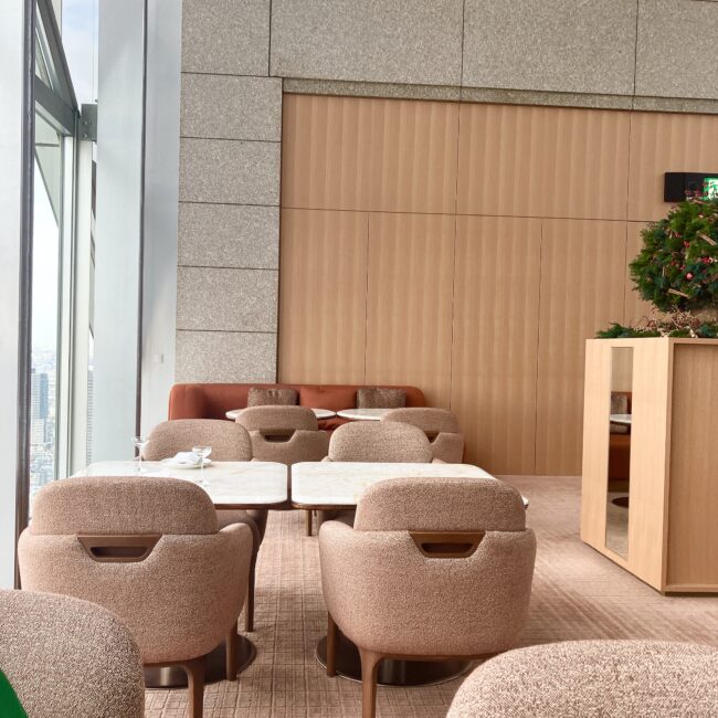 窓際から少し離れたテーブル席のレイアウト。落ち着いたトーンの椅子と、壁面の木目調のパネルが洗練された大人の空間を演出している。