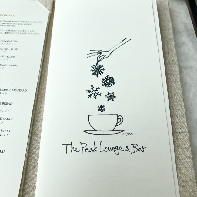 パークハイアット東京「ピークラウンジ」のティーメニューの表紙。ティーカップの上に雪の結晶が舞い落ちる繊細なイラストと、"The Peak Lounge & Bar" の手書きロゴが描かれている。