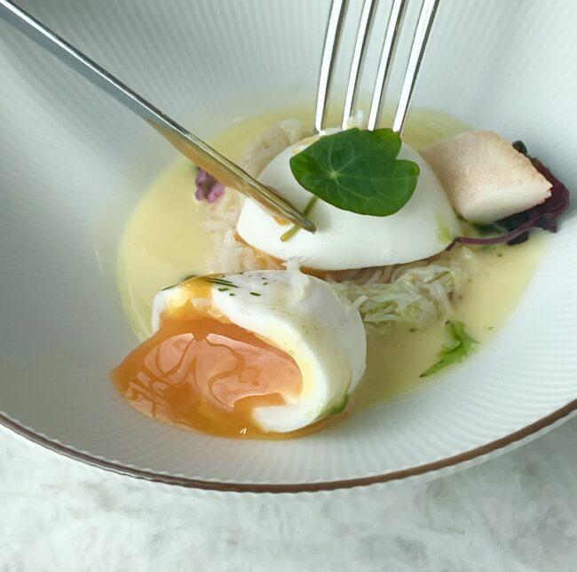 ポーチドエッグにフォークが入り、中から鮮やかなオレンジ色の黄身がとろりと溢れ出す瞬間のクローズアップ写真。