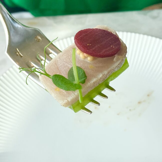 フォークですくい上げられた寒鰤の炙り。上に乗ったビーツの深い赤とマスタードの実、緑のハーブが、素材の鮮度を際立たせている。