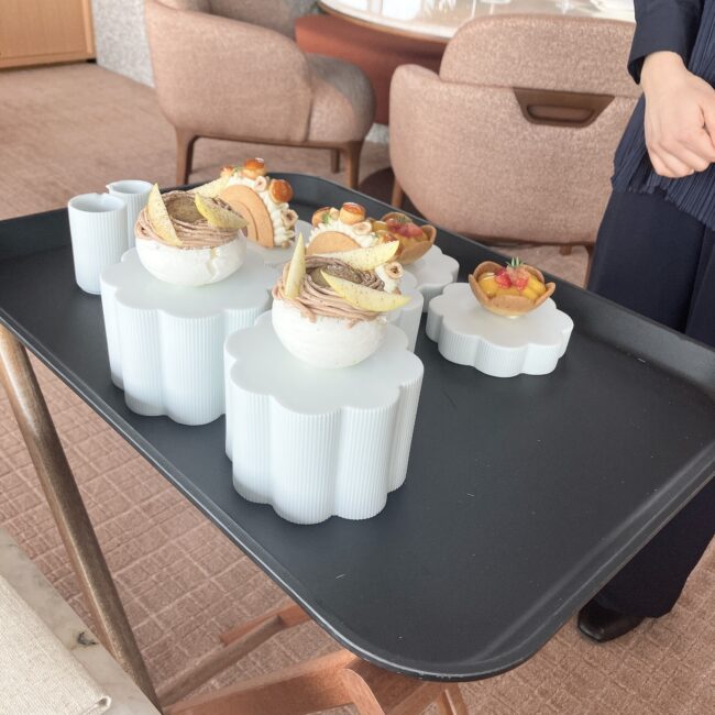 スタッフがトレイに載せて運んできた、高さの異なる白い陶器の台座と、その上に美しく盛り付けられたジュリアン・ペリネのスイーツたち。