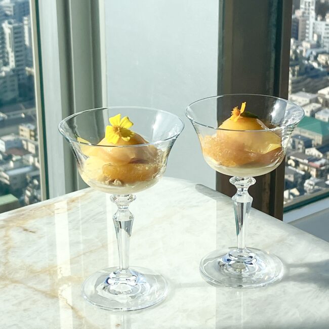 透明なグラスにマンダリンシャーベットとシトラスクリームが。バニラビーンズの粒が見える濃厚なクリームと、氷の結晶を感じるみずみずしいシャーベットの質感の対比。鮮やかな黄色のエディブルフラワーが添えられている。