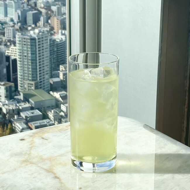 パークハイアット東京の高層階からの眺望を背景に置かれた、ロンググラス入りのアイスティー。シングルオリジンティーをアイスで楽しむ贅沢な様子。