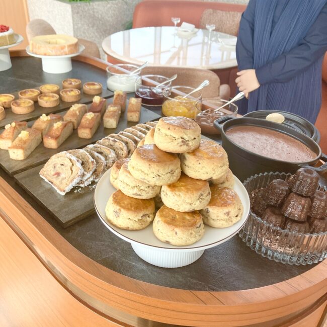 パークハイアット東京「ピークラウンジ」の新サービス、木製ワゴン「CAKES FROM THE TROLLEY(トローリー)」。山盛りに積まれた焼きたてのスコーンを中心に、カヌレ、マドレーヌ、タルト、シュトーレンなどの焼き菓子が美しく並べられている。奥にはジャムやハニーなどのコンディメントも用意されている。