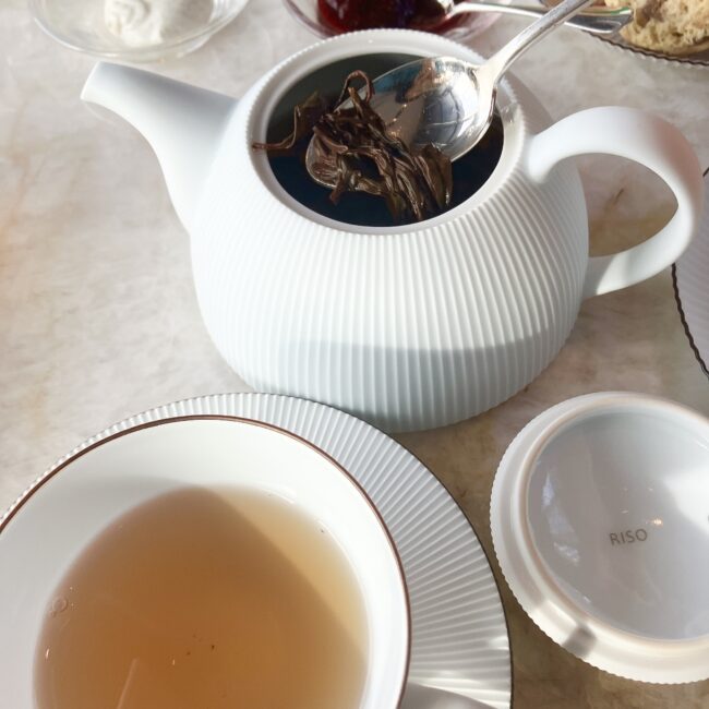 パークハイアット東京の新しい白いティーポットの中で、大きく開いた「お茶のカジハラ」のべにふうき紅茶の茶葉。スプーンですくい上げた茶葉は、黒々として力強い一芯二葉の形を残している。