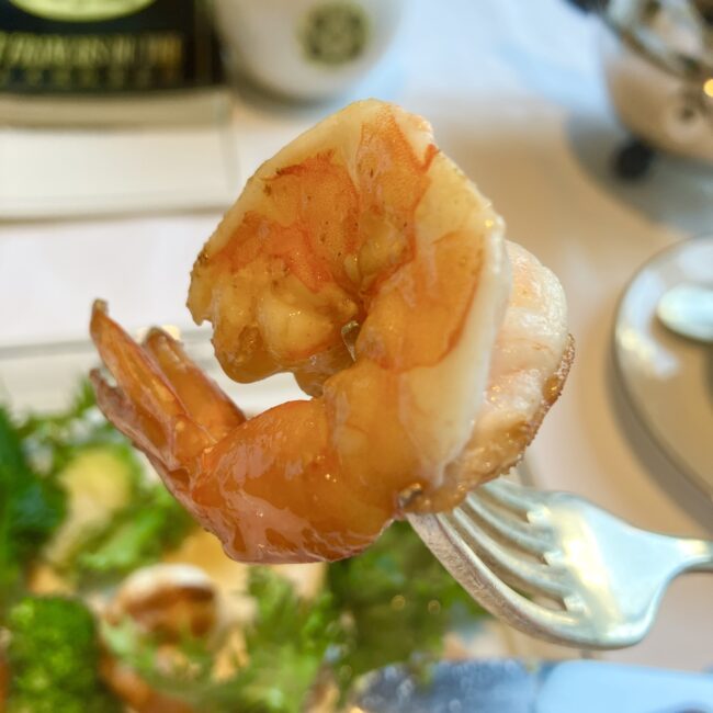 フォークに刺した天使の海老のアップ。香ばしく焼き上げられた表面とソースの艶が強調されている。