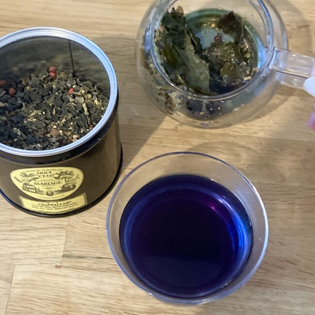 マリアージュフレールの紅茶缶「チャイワラ (CHAIWALLAH)」と、ガラスの急須で茶葉が抽出されている様子。グラスに注がれた水色は鮮やかな濃い紫色をしている。