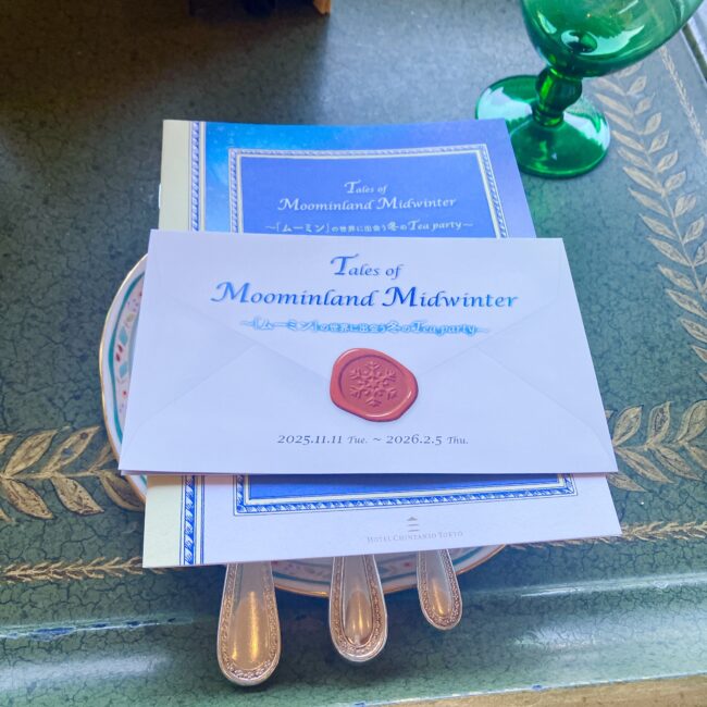 椿山荘×ムーミンコラボ専用のアフタヌーンティーメニューと、招待状セット。雪の結晶が刻印された赤い封蝋風シールで留められた封筒が、グリーンのアンティーク調トレイに美しく配置されている。