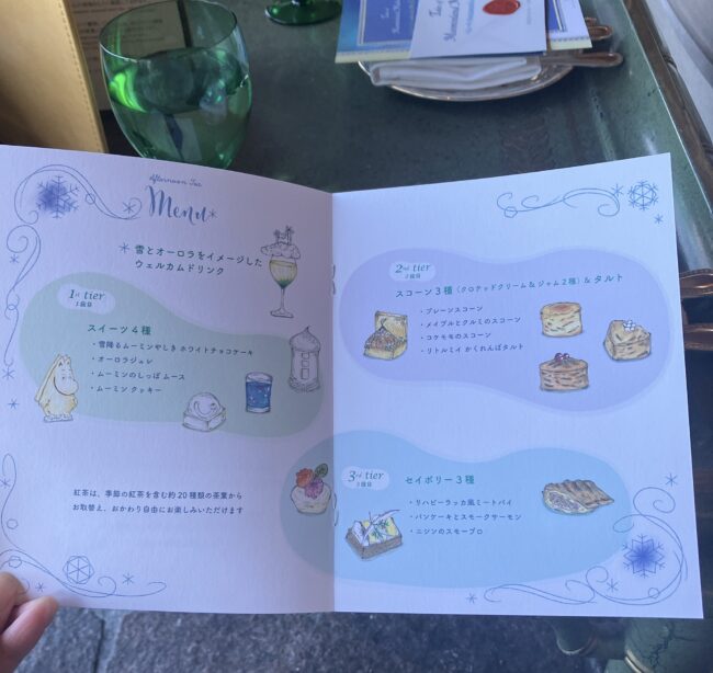 「ムーミン谷の冬」アフタヌーンティー専用のイラスト入りメニュー表。左ページにスイーツ4種、右ページにスコーンとセイボリーの詳細が、繊細な水彩画風イラストと共に記載されている。