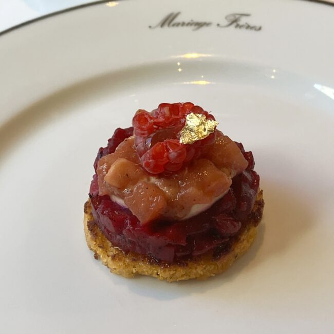 「ノエル ロワイヤル」の紅茶を使った、スモークサーモンとビーツの「ビジュー」。 キャプション: BIJOU（ビジュー）：その名の通り宝石のような一品。スモークサーモンとビーツの赤いグラデーションに、金箔が輝きます。
