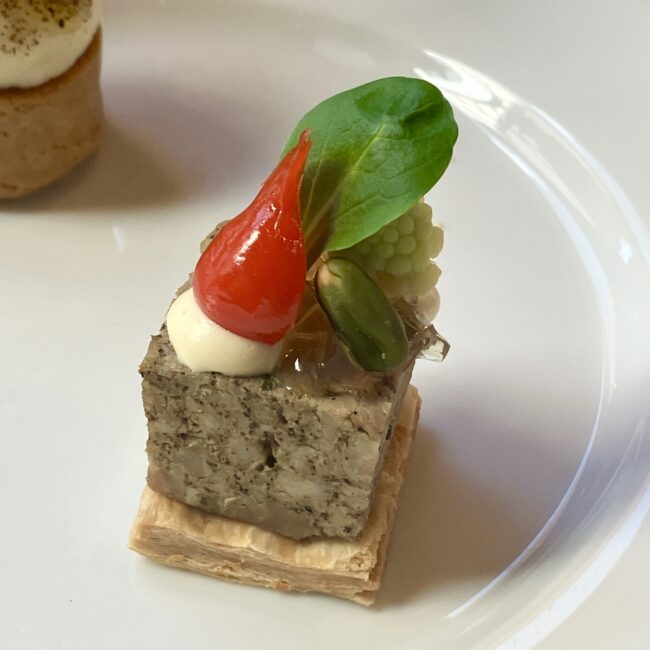 「アレクサンドラ ダヴィッドネール」の紅茶を使った仔牛のテリーヌ。 テリーヌの上には、ロマネスコの緑、ピスタチオ、そして妖精の帽子のような赤いプティポワプロン（ミニパプリカ）が飾られ、食べるのが惜しいほどの可愛らしさです。