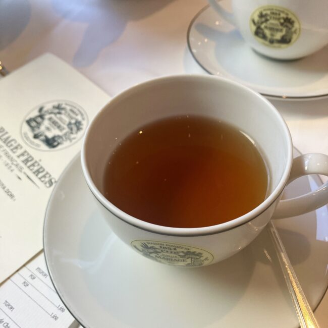 マリアージュフレールのフレーバードティー「アールグレイ ビューティー (EARL GREY BEAUTY) Ref. T80061」。白いティーカップに注がれた紅茶の水色は深みがあり、ロゴ入りのソーサーに乗っている。