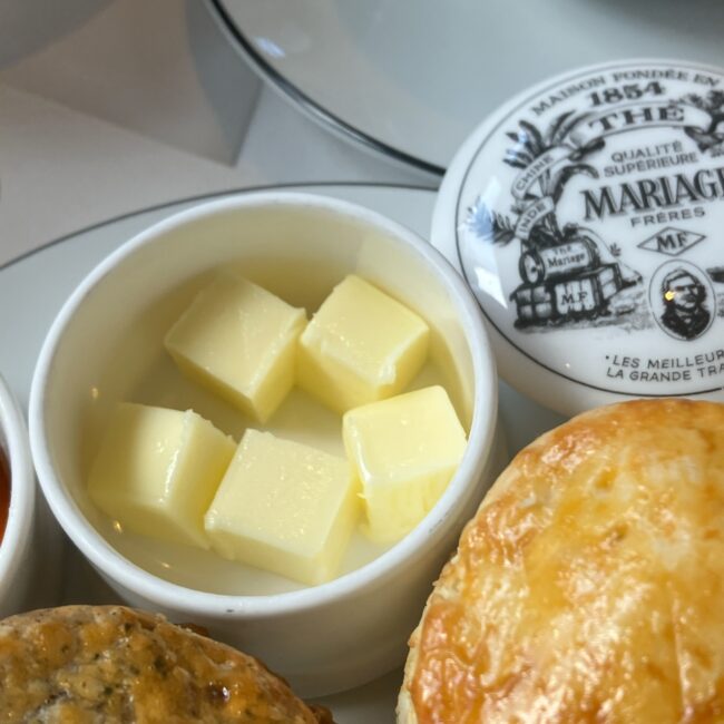マリアージュフレール銀座松屋通り店のアフタヌーンティーで提供されるフランス産バター。白磁の容器に入ったキューブ状のバターと、伝統的なロゴが入った蓋、手前には焼きたてのスコーンの一部が写っている。