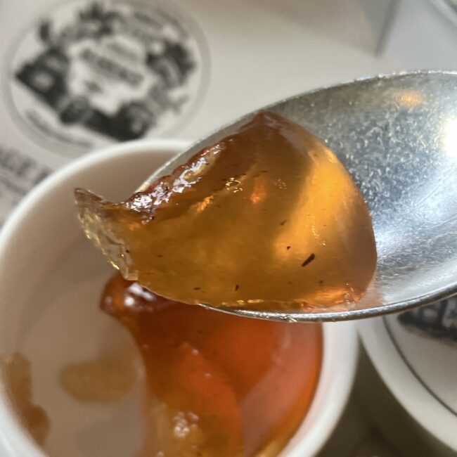 スプーンですくったマリアージュフレールの紅茶のジャム「ノエル アムール」。琥珀色のゼリーの中に、スパイスと茶葉の粒が閉じ込められ、光を受けて宝石のように輝いている。