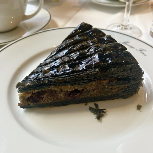 マリアージュフレールの期間限定スイーツ「マルコポーロのガレット・デ・ロワ」。漆黒のパイ生地は表面が艶やかにキャラメリゼされ、美しい層を描いている。白い皿の上で圧倒的な存在感を放つ1カット。